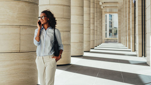 Young smiling businesswoman talking on smart phone while walking in corridor