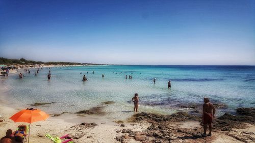 People at beach against clear blue sky