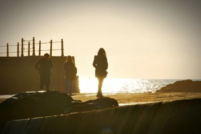 Silhouette men on beach against sky during sunset