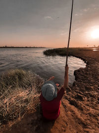 Rear view of woman standing at beach against sky during sunset