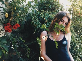 Portrait of young woman standing by plants at yard