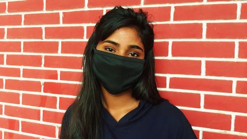 Portrait of beautiful woman standing against red brick wall wearing mask 