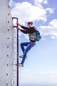 Side view of man climbing on ladder against cloudy sky