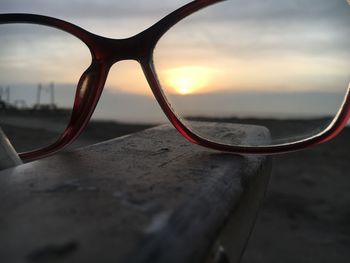 Surface level of sunglasses on beach against sky during sunset