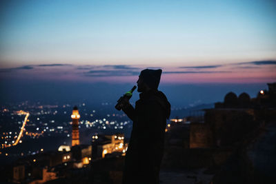 Silhouette man having wine against sky at dusk