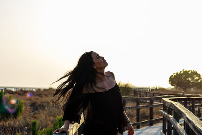 Young woman standing on walkway over field against clear sky