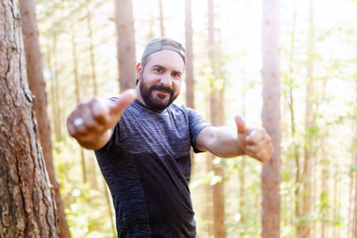 Portrait of man standing by tree trunk in forest