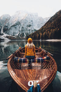 Rear view of woman sitting on snowcapped mountain by lake