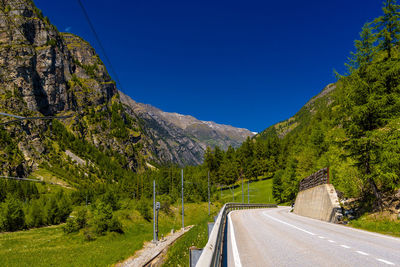 Road amidst trees and mountains against clear blue sky