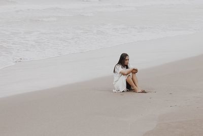 Sad young woman sitting on sand against sea at beach