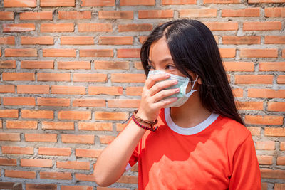 Portrait of a young woman drinking water against brick wall