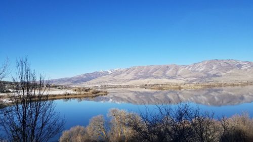 Scenic view of lake and mountains against clear blue sky