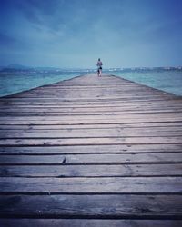 Rear view of woman walking on pier against sky