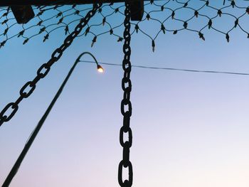 Low angle view of lighting decoration and metal chain by street light against clear sky