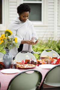 Woman photographing food through phone at table in backyard