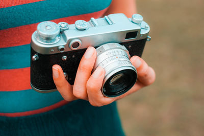 Midsection of woman holding camera while standing outdoors