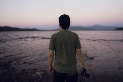 Rear view of man standing on shore at beach during sunset