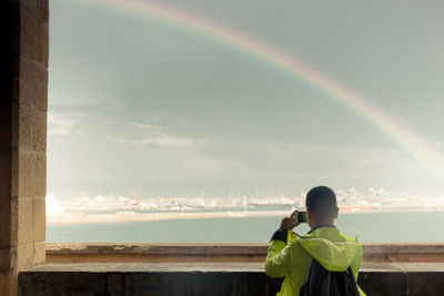 Person in the rain photographing a rainbow over the city of naples