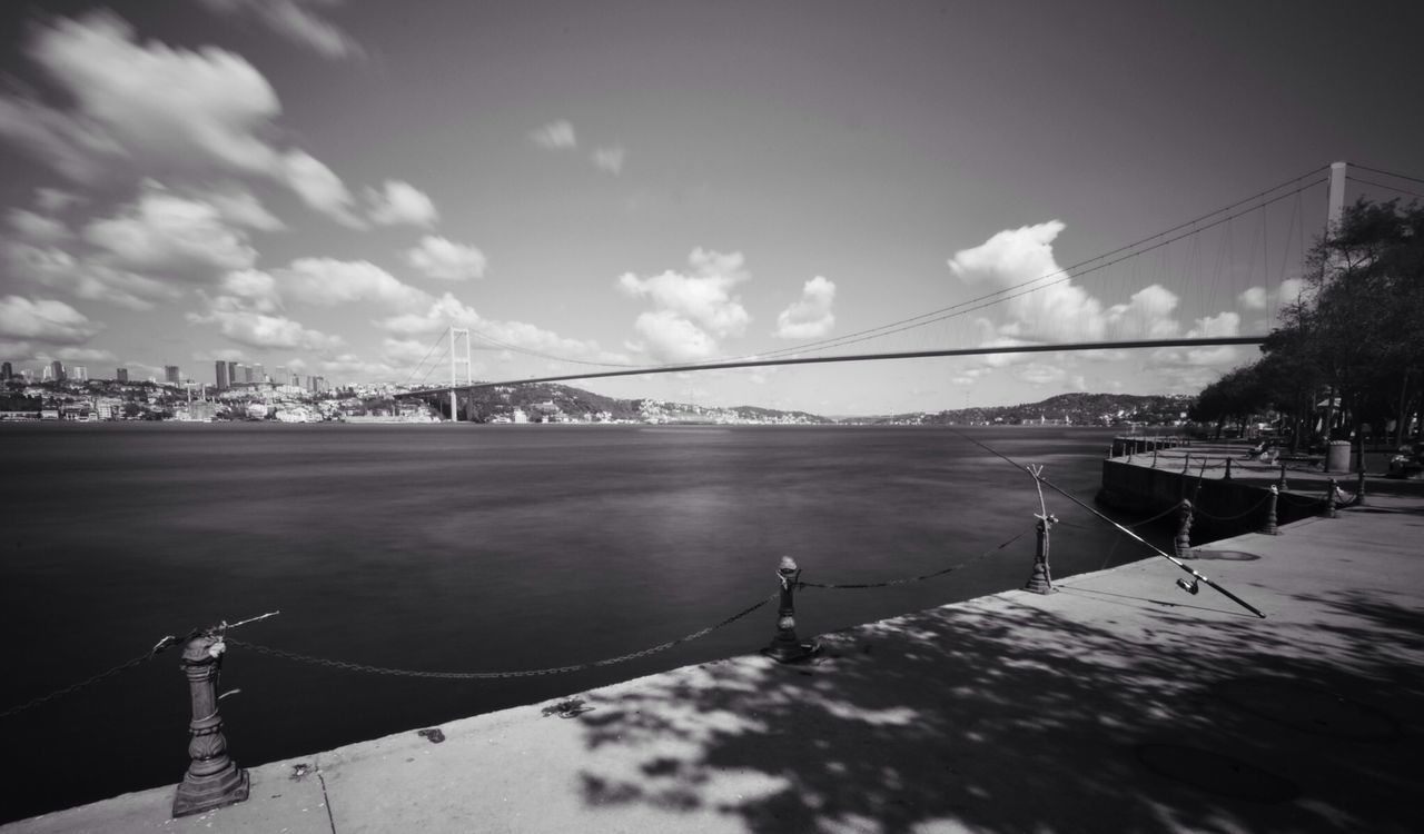 sky, built structure, architecture, connection, railing, building exterior, transportation, bridge - man made structure, outdoors, sunlight, day, no people, water, river, cloud, cloud - sky, pole, fence, metal, nature