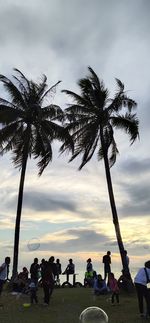 People by palm trees against sky during sunset