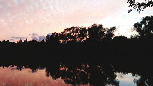 Silhouette trees by lake against sky during sunset