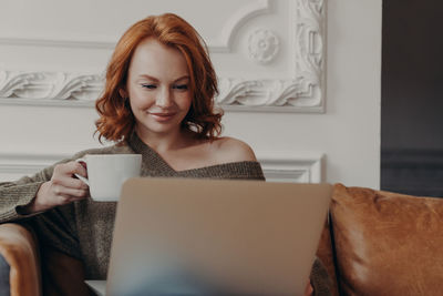 Close-up of smiling woman using laptop sitting at home