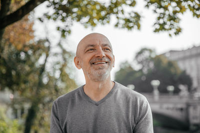 Happy senior man in grey sweater sitting in a park, smiling warmly