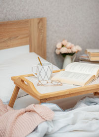 Cup of coffee, book and glasses on bed with soft blanket indoors