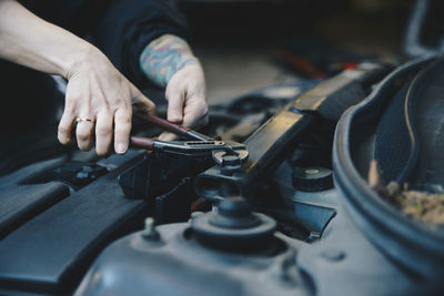Cropped image of female mechanic tightening nut on car engine with wrench