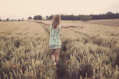 Rear view of girl standing on field against sky