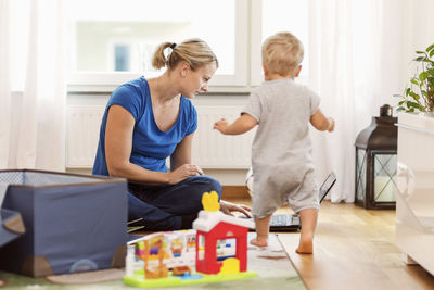 Baby boy walking towards mother using laptop at home