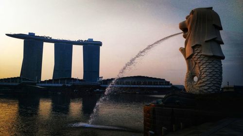 View of city by river against sky during sunset