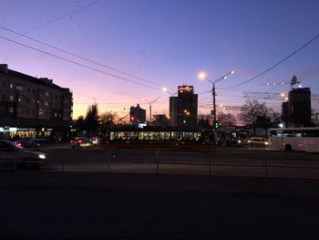 Illuminated city street against sky at sunset