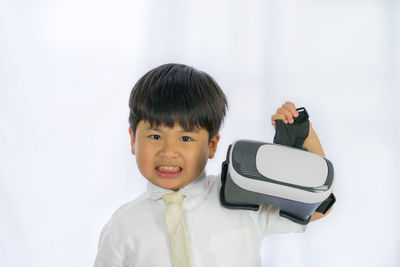 Portrait of boy holding virtual reality simulator against white background