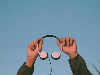 Low angle view of hand against blue sky , holding headphone