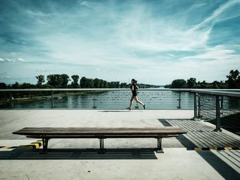 Man standing on railing by lake against sky