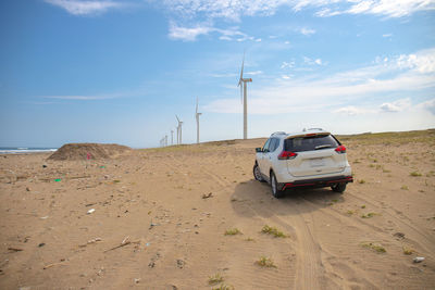 Cars on river side by land against windmills