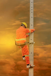 Man working on ladder against orange sky