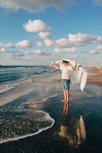 Full length of boy standing with scarf on shore against sky