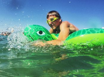 Shirtless boy swimming in sea with inflatable raft