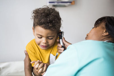 Female pediatrician examining boy's ear in medical clinic