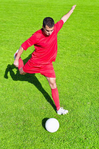 High angle view of man kicking soccer ball on field during sunny day