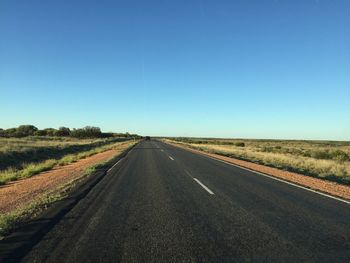 Road amidst field against clear blue sky