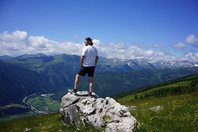 Man standing on rock looking at mountains against sky