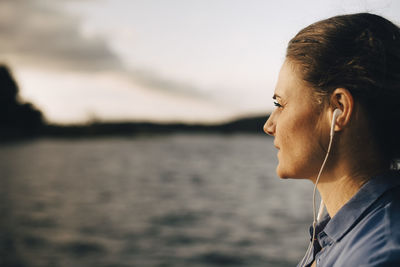 Close-up of thoughtful woman listening music through headphones by lake in summer vacation