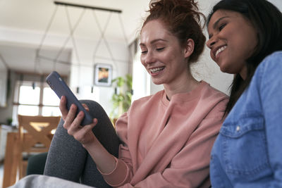 Smiling female friends looking at smart phone at home