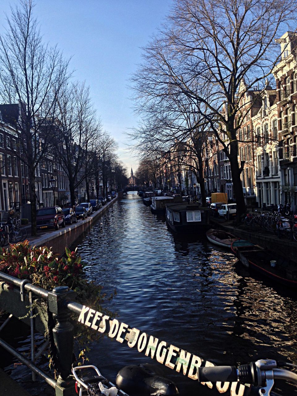 transportation, tree, water, mode of transport, bare tree, nautical vessel, canal, boat, river, moored, text, railing, built structure, western script, bridge - man made structure, day, branch, nature, outdoors, architecture