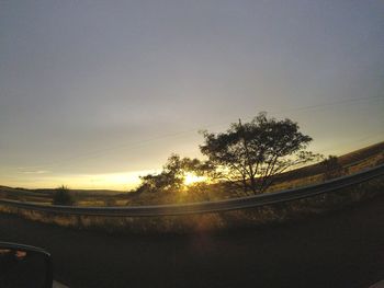 Road by trees against sky during sunset