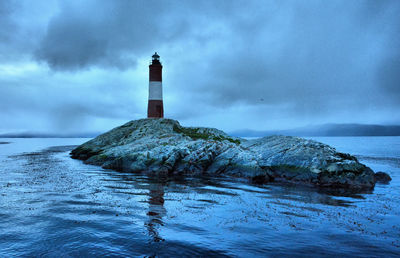 Lighthouse on rock by sea against sky