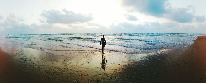 Panoramic view of silhouette man standing on sea shore against sky